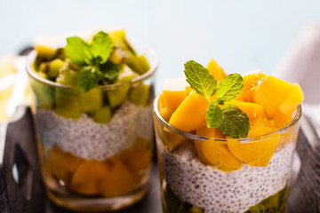Dietetic dessert in the form of a fresh fruit salad with kiwi and peach with chia seeds and yoghurt served in a glass.