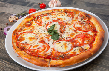 Italian pizza with tomato topped with melted golden cheese, herbs and basil on wood table
