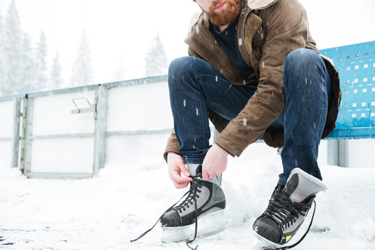 Man Tying Shoelace On Ice Skates Outdoors