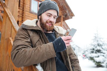 Smiling man standing and using smartphone outdoors in winter