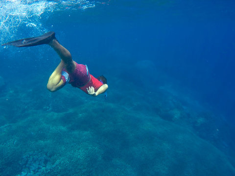Man in red swimsuit dives to the coral reef
