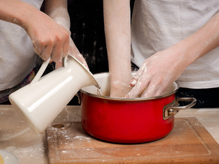 The process of kneading dough. human hands Close. The dough is made of flour. Cookware - red pot, white pitcher. Hand poured water from a jug