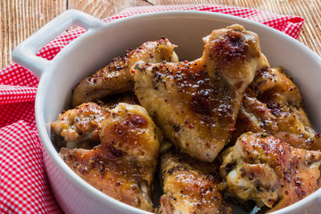 Roasted chicken wings in white baking dish. Cooked with sauce from mustard, honey and soy sauce.