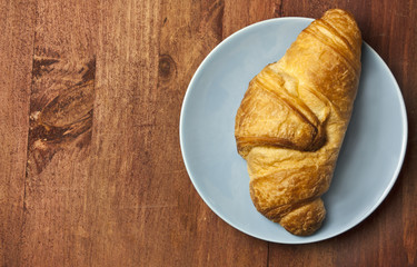 Croissant on blue plate, on wooden board texture, with copyspace