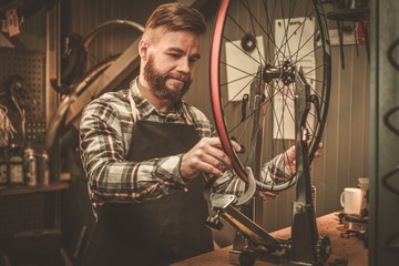 Stylish bicycle mechanic doing his professional work in workshop.