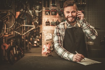 Obraz na płótnie Canvas Stylish bicycle mechanic takes order by phone in his workshop.