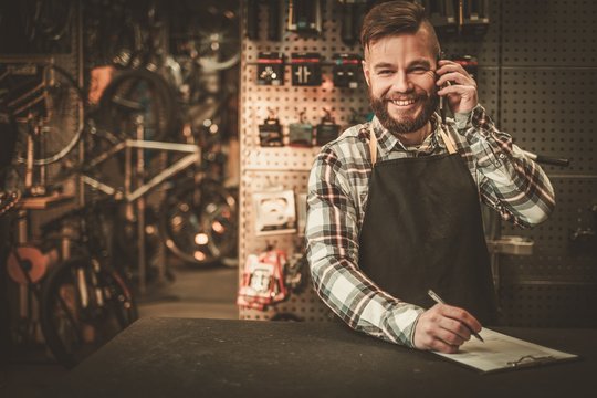 Stylish bicycle mechanic takes order by phone in his workshop. - Powered by Adobe