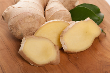Ginger root slices with green leaves on wooden table.