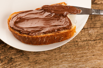 Slice of bread with sweet chocolate nougat spread on white plate