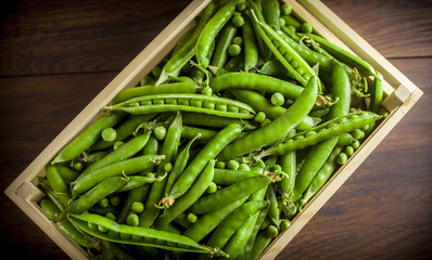 Green peas group overhead in small wooden box on brown wooden table in studio