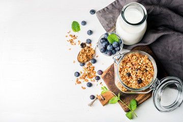 Healthy breakfast ingrediens. Homemade granola in open glass jar, milk or yogurt bottle, blueberries and mint