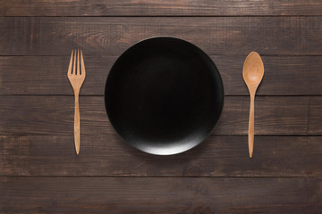 Black dish, fork and spoon on the wooden background. Top view