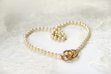 Heart of pearl necklace with two golden rings resting on white wedding lace