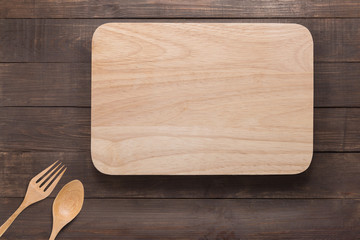 Cutting board, spoon and fork on the wooden background