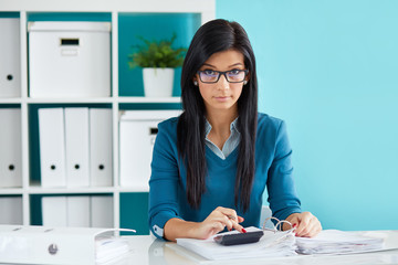 Woman with glasses calculates tax at desk