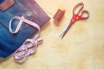 Tape measure, scissors, needle and thread to sew jeans wooden table