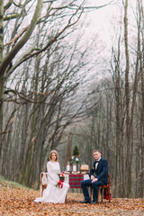 Wedding couple sitting at the holiday table in autumn forest