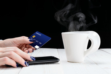 Woman sitting at table and pays the purchase through smartphone