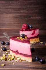 Piece of delicious raspberry cake with fresh raspberries, blueberry, currants and pistachios on shovel, wooden background. Free space for your text.