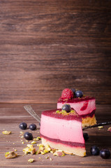 Obraz na płótnie Canvas Piece of delicious raspberry cake with fresh raspberries, blueberry, currants and pistachios on shovel, wooden background. Free space for your text.