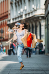 Young woman jumping at the street happy after shopping 