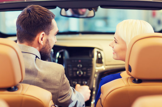 happy couple sitting in car at auto show or salon