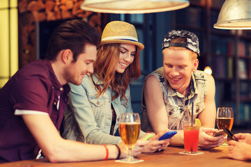 happy friends with smartphones and drinks at bar