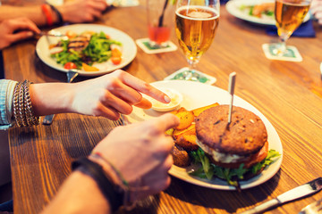 close up of friends hands sharing burger at bar