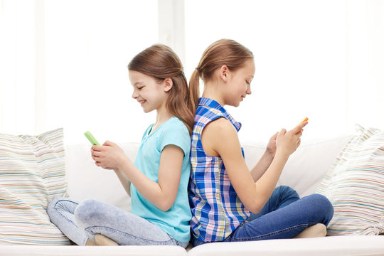 happy girls with smartphones sitting on sofa