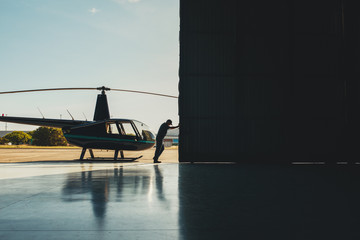 Pilot opening the helicopter hangar door. - obrazy, fototapety, plakaty
