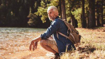 Senior male hiker relaxing by a lake and admiring the view