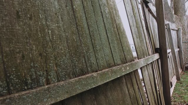 camera slowly moves toward an opening in a broken fence. Side angle, broken and moldy old fence
