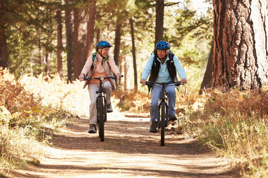 Senior couple mountain biking on forest trail, California