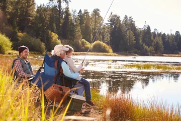 Gordijnen Grandad teaches his grandson to fish at a lake, dad watching © Monkey Business