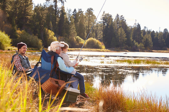 Grandad teaches his grandson to fish at a lake, dad watching