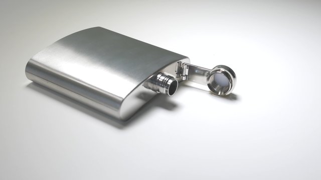Dolly pan shot of a hip flask on a white table.
