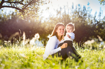 Mother holding her little son, sitting on the grass