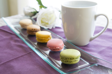 Macaroon colorati su vassoio decorativo di vetro con tazza e rosa bianca su tovaglia viola