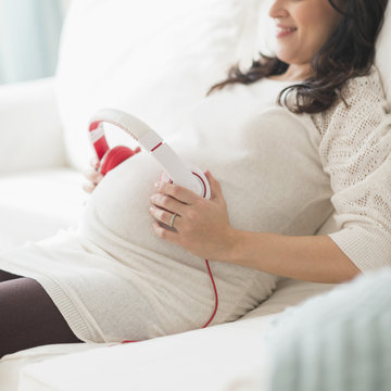 Pregnant Hispanic woman holding headphones on belly