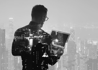 Double exposure young bearded businessman wearing black shirt and holding modern notebook hands. Panoramic view contemporary night city background. Black, white. Horizontal mockup 