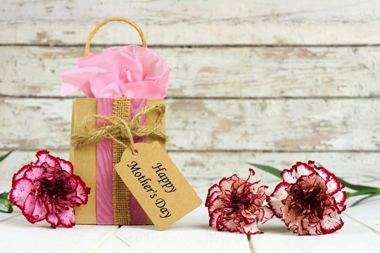 Mothers Day gift bag with tag and beautiful carnation flowers against a rustic white wood background