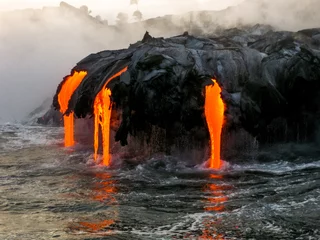 Fotobehang Sea view of Kilauea Volcano in Big Island, Hawaii, United States. A restless volcano that has been in business since 1983. Shot taken at sunset when the lava glows in the dark as jumps into the sea. © bennymarty