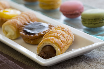 Pasticcini, cannoncini, Macaroon su vassoi bianco e di vetro e tovaglia di lino 
