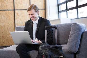 Happy businessman sitting on sofa and using laptop 
