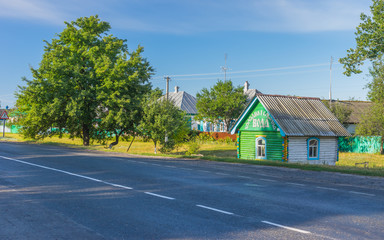 Fototapeta na wymiar Summer landscape with big pear-tree and draw-well as a small wooden house at roadside in Lyubka village, Sumskaya oblast, Ukraine