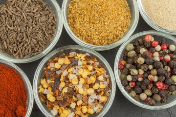 Various kinds of spices in glass bowls on a slate background. Preparation for cooking spicy food. Spices for master cook. The spice trade. Sale of spices in the kitchen.
