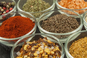 Various kinds of spices in glass bowls on a slate background. Preparation for cooking spicy food. Spices for master cook. The spice trade. Sale of spices in the kitchen.
