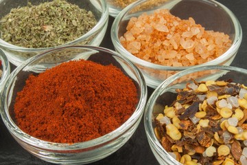 Various kinds of spices in glass bowls on a slate background. Preparation for cooking spicy food. Spices for master cook. The spice trade. Sale of spices in the kitchen.
