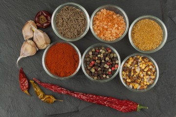 Various kinds of spices in glass bowls on a slate background. Preparation for cooking spicy food. Spices for master cook. The spice trade. Sale of spices in the kitchen.
