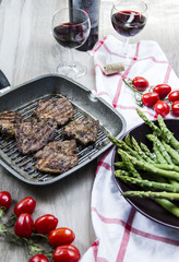 Grilled lamb with green asparagus, grill pan, red vine, wood background.